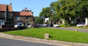 Picture of Osmotherley village green, showing the village cross and stone table (July 2021)